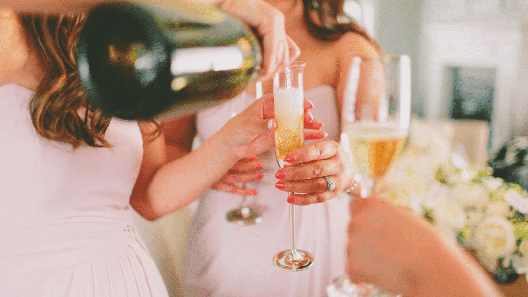Champagne being poured into a flute held by a woman in a white dress at a celebration.