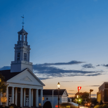 Small town street with a white church and a tall steeple under a twilight sky.